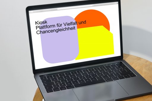 Laptop auf einem Stuhl mit aufgeklapptem Bildschirm, zeigt die Startseite von Kiosk Plattform für Vielfalt und Chancengleichheit