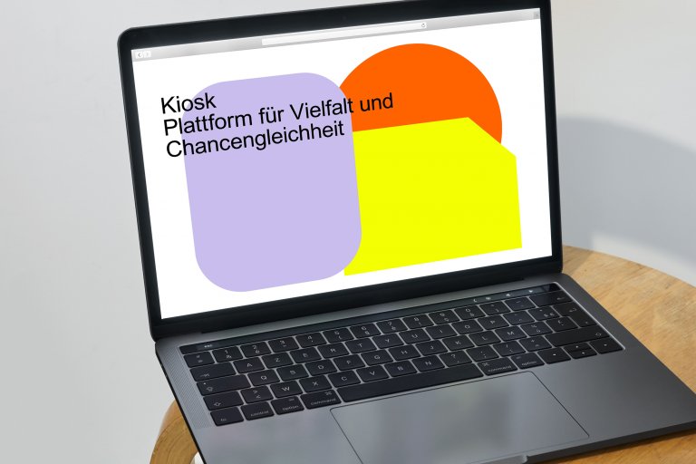 Laptop auf einem Stuhl mit aufgeklapptem Bildschirm, zeigt die Startseite von Kiosk Plattform für Vielfalt und Chancengleichheit