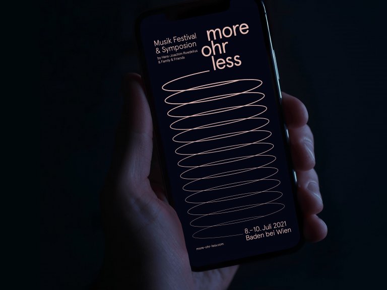Eine Hand hält ein Handy mit der Startseite von More Ohr Less